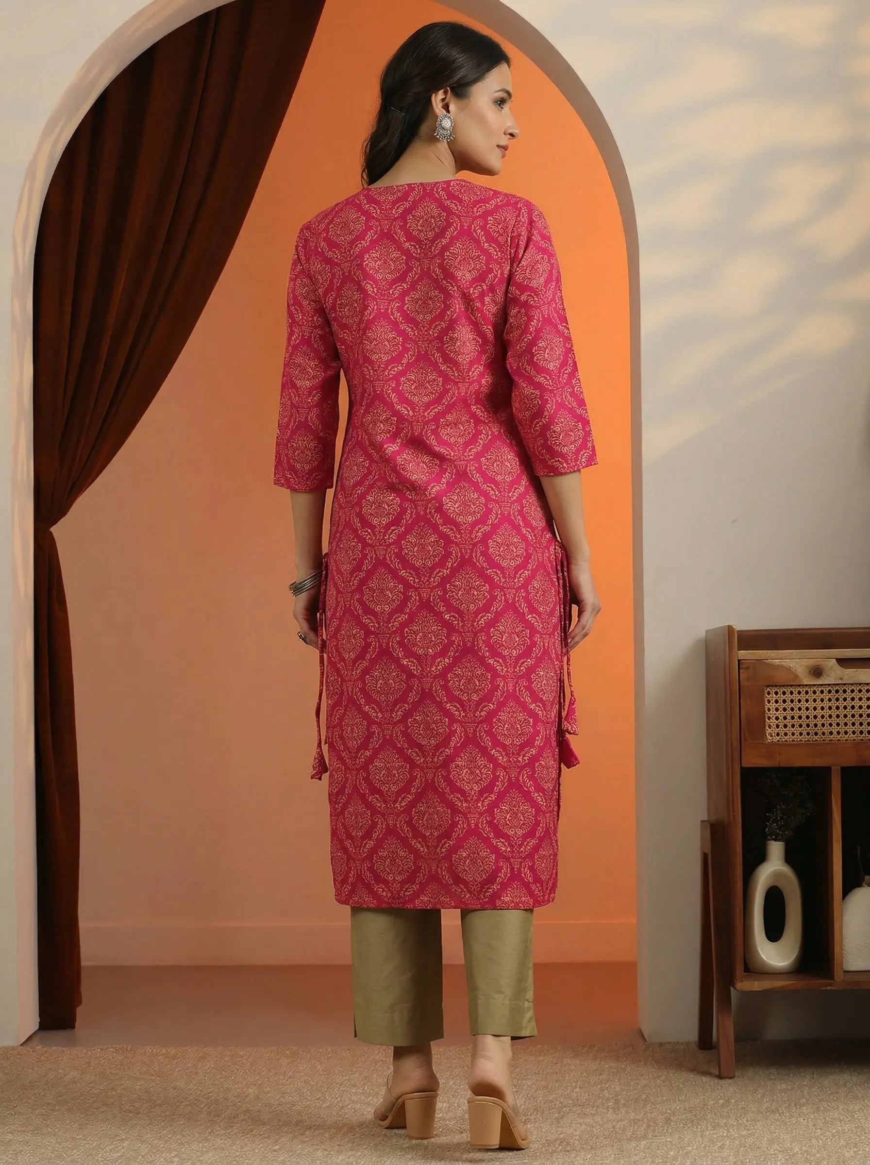 Woman wearing a pink traditional outfit standing in a room with an orange wall.